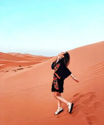 a woman walking on a sand dune in the desert at Majestic Dunes Luxury Camp in Merzouga