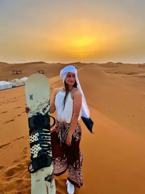 a woman standing in the desert with a snowboard at Majestic Dunes Luxury Camp in Merzouga