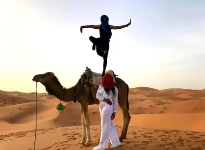 a man standing next to a camel in the desert at Majestic Dunes Luxury Camp in Merzouga