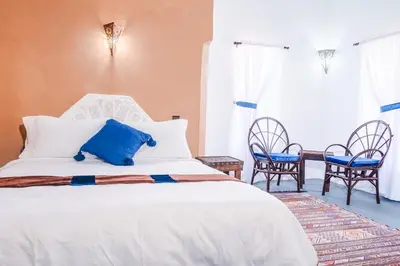 a bedroom with a white bed with two chairs and a table at Kasbah Tiziri in Kalaat MGouna