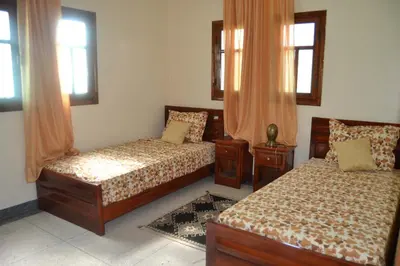 a bedroom with two beds and two windows at Résidence Ayour in Ouarzazate