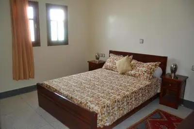 a bedroom with a bed with two night stands and two windows at Résidence Ayour in Ouarzazate