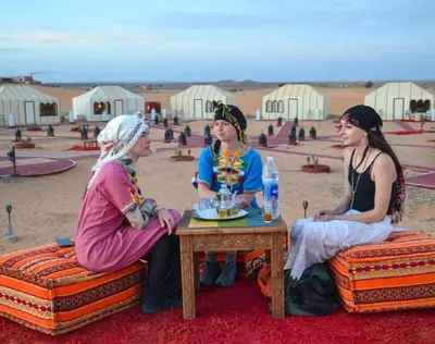 three women sitting around a table in the desert at Merzouga Camel Ride & Overnight Desert Camp in Merzouga