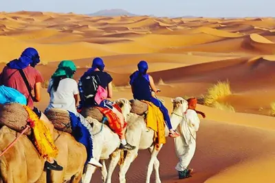 a group of people riding camels in the desert at Merzouga Camel Ride & Overnight Desert Camp in Merzouga