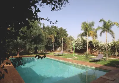 a swimming pool with two chairs and palm trees at Maison d'Hôtes à Marrakech in Marrakech