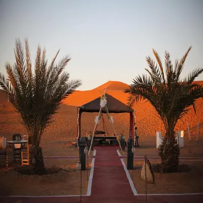 a tent in the middle of a desert with two palm trees at abja luxury camp in Merzouga