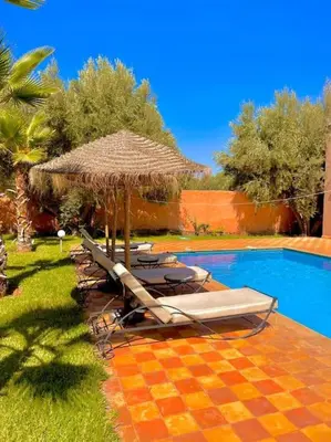 a group of lounge chairs and an umbrella next to a pool at Villa1 des tortues Marrakech in Aït Zat