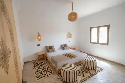 a white bedroom with a bed and two chairs at Dar Diafa in Merzouga