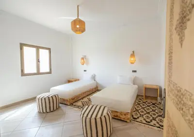 a white room with two beds and a chair at Dar Diafa in Merzouga