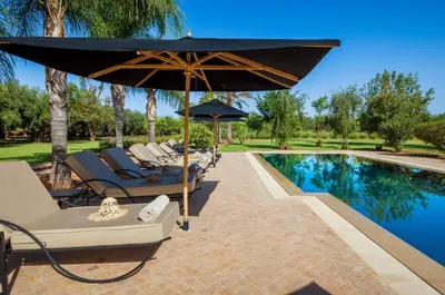 a pool with chairs and an umbrella next to a swimming pool at Maidan El Arsa in Marrakech