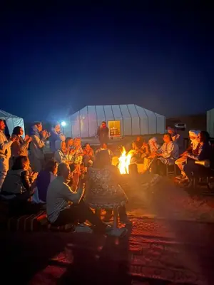 a group of people sitting around a fire at night at Touareg Desert Camp Erg Chigaga in El Gouera