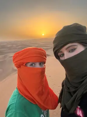 two women standing on the beach with the sunset in the background at Touareg Desert Camp Erg Chigaga in El Gouera