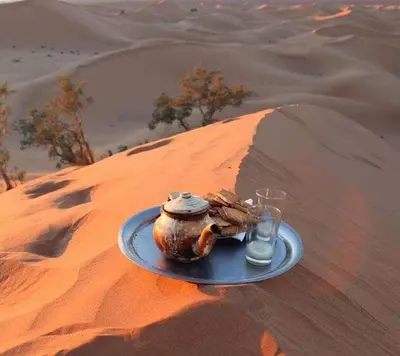 a plate with a pot and a glass in the desert at voyageur m'hamid Ghislaine in Tâlhâ