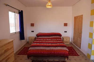 a bedroom with a bed with a striped blanket on it at Dar Tiniri - Guest House - Zagora in Arhla Ou Drar