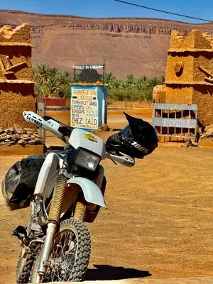 a motorcycle parked in front of a sign in the desert at Auberge Dar Lajdoud in Tafraoute Sidi Ali