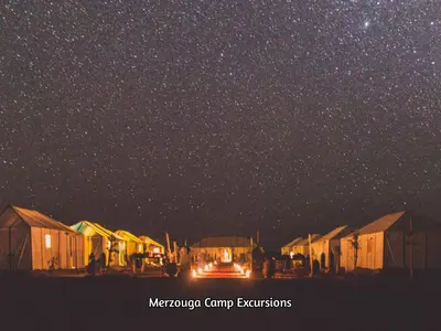 a starry night with a truck parked under a cluster of buildings at Merzouga Camp Excursions in Merzouga