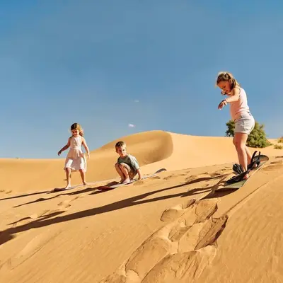 three children playing on a sand dune in the desert at Best Luxury Camp in Merzouga