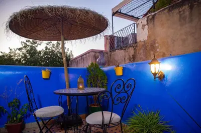 a patio with a table and chairs and a blue wall at Riad LalaMoune in Fès