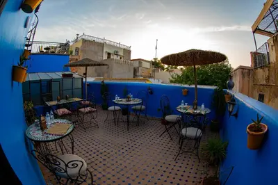 a patio with tables and chairs and a blue wall at Riad LalaMoune in Fès