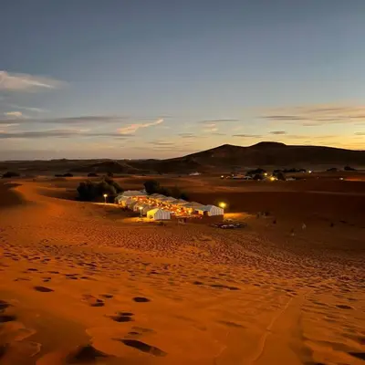 a desert with a group of buildings in the desert at Merzouga Berber Camps in Merzouga
