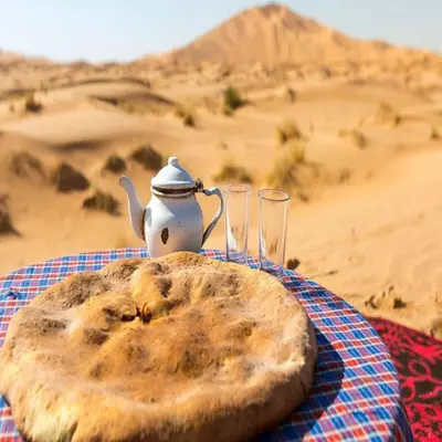 a plate of bread and two glasses on a table in the desert at Merzouga Berber Camps in Merzouga