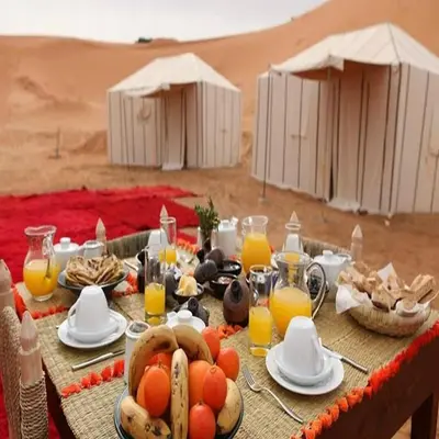 a table in the desert with food and orange juice at Merzouga Berber Camps in Merzouga
