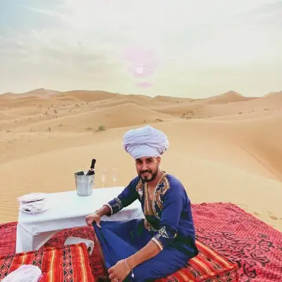 a man sitting at a table in the desert at Merzouga Berber Camps in Merzouga