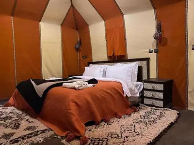 a bedroom with a bed with an orange blanket and a rug at Sahara Elegance Camp in Merzouga