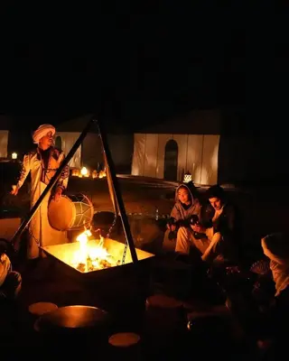 a group of people sitting around a fire in a tent at Aurum Dunes Luxury Camp in Merzouga