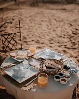 a table with food and drinks on the beach at Aurum Dunes Luxury Camp in Merzouga