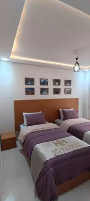 a bedroom with two beds and pictures on the wall at APPART-HOTEL La MAISON ATTAWBA 2 in Beni Mellal