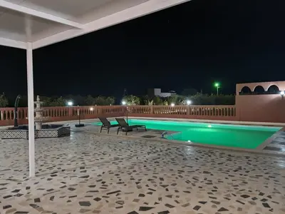 a swimming pool at night with benches and an umbrella at Villa des Oliviers MEKNES in Meknès