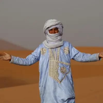 a woman in a blue dress with her arms outstretched at Luxurious Desert Camp in Merzouga