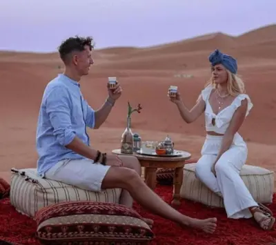 a man and woman sitting in the desert holding wine glasses at Luxurious Desert Camp in Merzouga