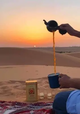 a person is pouring honey into a blue cup on the beach at Ecolodge Le désert in Kasr Bounou