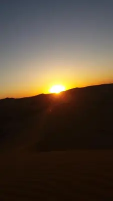 a sunset in the desert with the sun setting in the horizon at Chez Belkacem in Merzouga