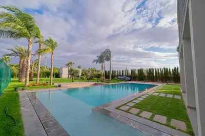 a swimming pool with palm trees next to a building at Villa vue atlas marrakech in Marrakech