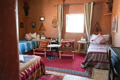 a bedroom with two beds and chairs and a window at Riad Paradise of Silence in Aït Ben Haddou