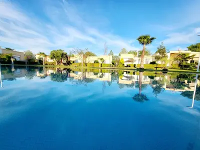 a large pool of water with houses and palm trees at Duplex Reposant avec piscine au Andalines Golf Royal Fès in Dar Ito Lahssene