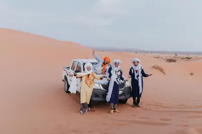 a group of people standing next to a car in the desert at Kam Kam Dunes in Merzouga
