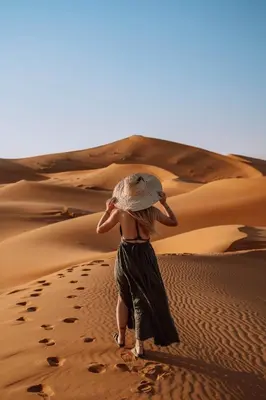 a woman walking in the desert with a hat on her head at Kam Kam Dunes in Merzouga