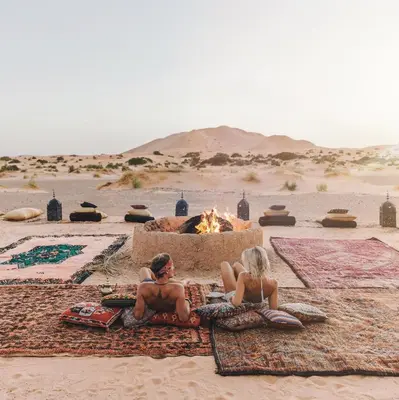 a man and woman sitting next to a fire in the desert at Kam Kam Dunes in Merzouga