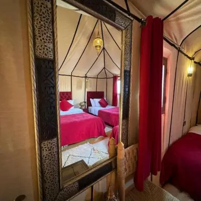 a mirror in a room with two beds with red sheets at desert tribe luxury camp in Merzouga