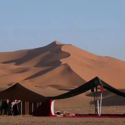 a sand dune with a tent in the desert at desert tribe luxury camp in Merzouga
