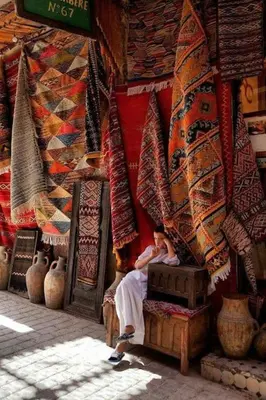 a woman sitting on a stool in front of a room with carpets at Appartement Atlas City Center 2 in Fès
