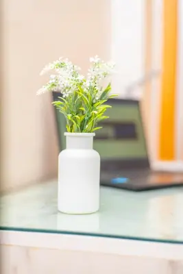 a white vase with flowers on a desk with a laptop at Familiale, raffinement et calme, entourée d'une vue sur le jardin - À proximité de l'aéroport et de Marjane in Fès