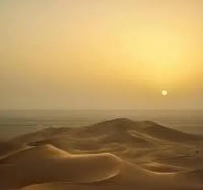 a desert with the sun rising over the ocean at Aaladdin luxury camp in Merzouga