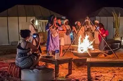 a group of people standing around a fire at Aaladdin luxury camp in Merzouga