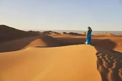 a woman standing on top of a sand dune in the desert at Aaladdin luxury camp in Merzouga
