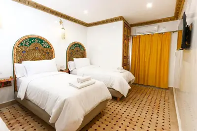 a bedroom with two beds with white sheets and yellow curtains at Dar Ibn Majdoub Lala aicha & Alia in Fès